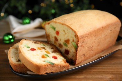 Photo of Delicious cake with candied fruits on wooden table against Christmas lights, closeup