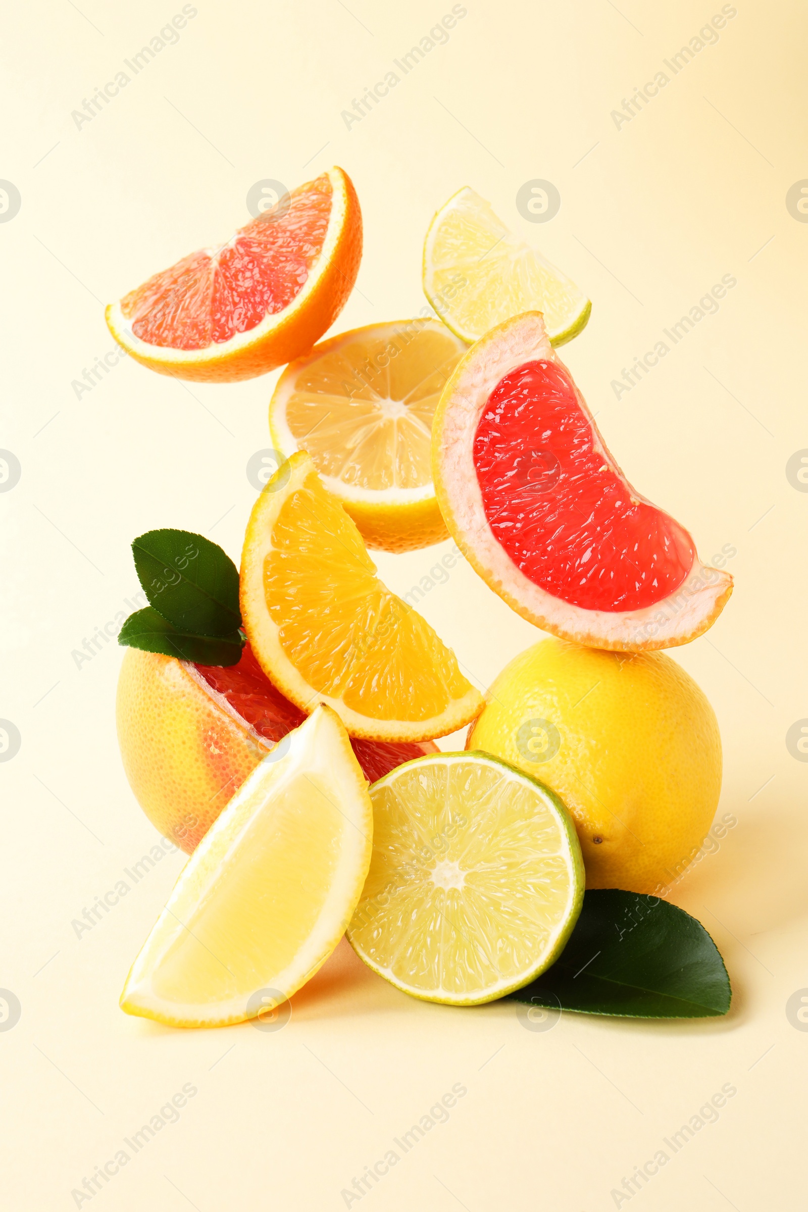 Photo of Fresh ripe citrus fruits and green leaves on beige background