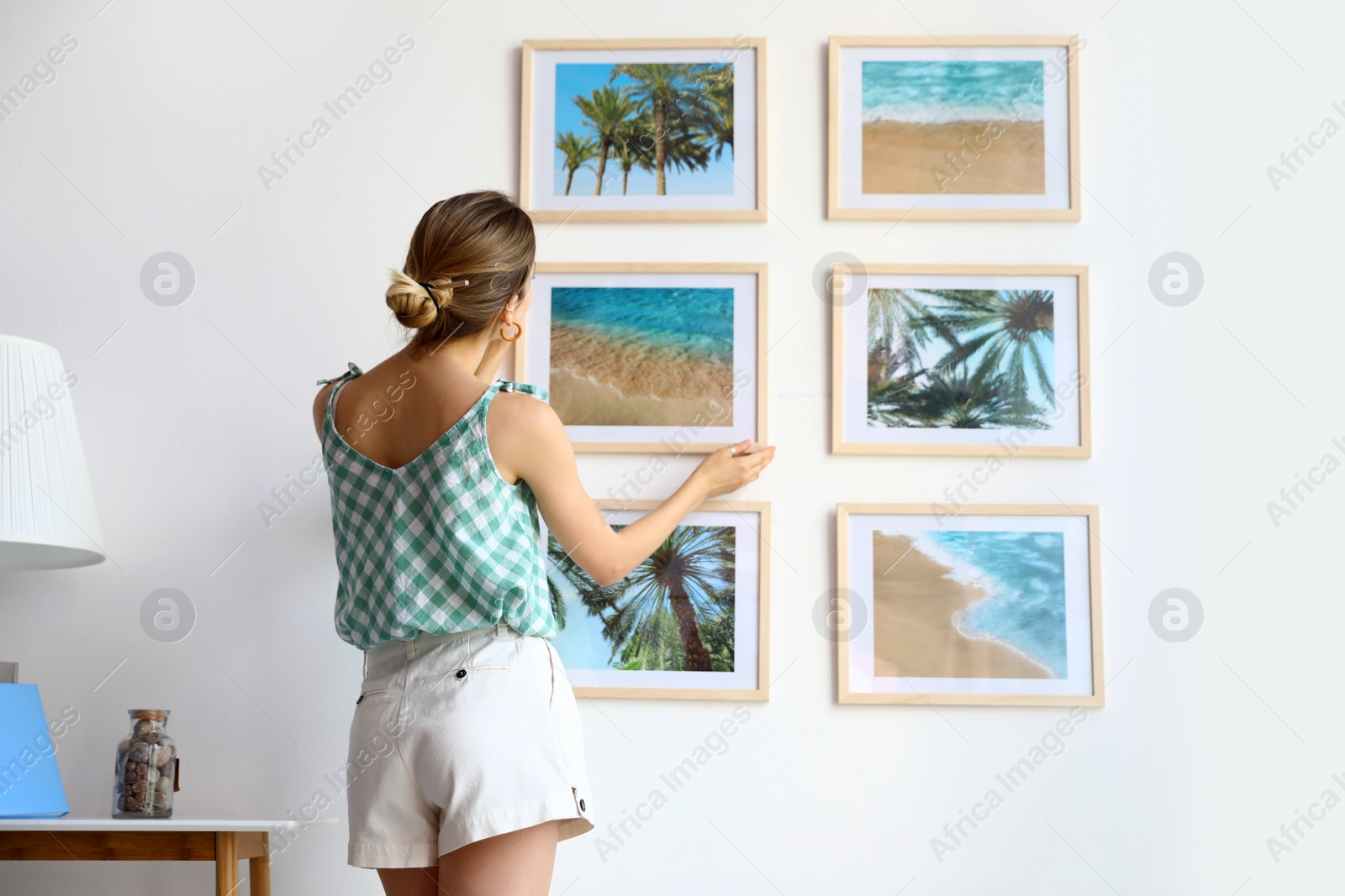 Photo of Female interior designer decorating white wall with pictures indoors