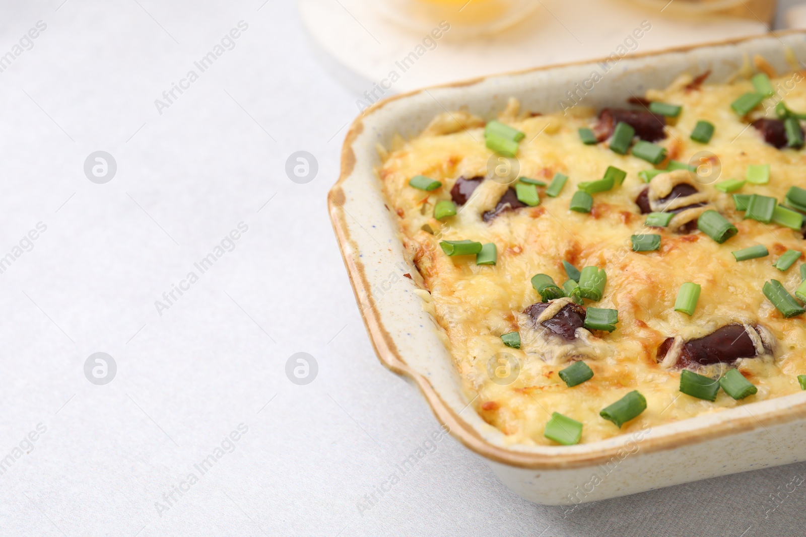 Photo of Tasty sausage casserole with green onions in baking dish on white table, closeup. Space for text