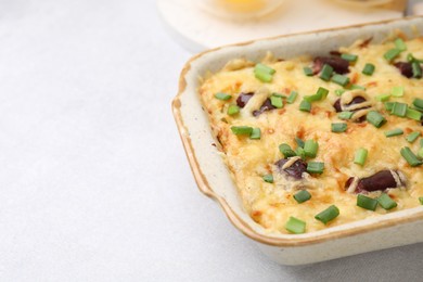 Photo of Tasty sausage casserole with green onions in baking dish on white table, closeup. Space for text