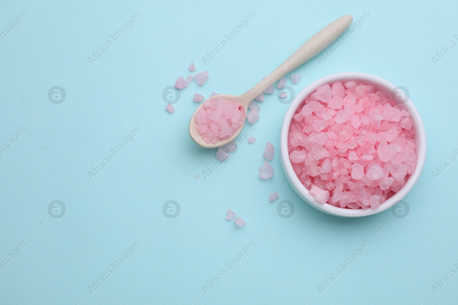 Photo of Bowl and spoon with pink sea salt on light blue background, flat lay. Space for text