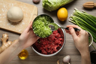 Photo of Woman adding chopped cabbage to gyoza filling at wooden table, top view