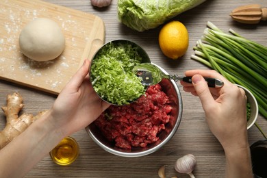 Woman adding chopped cabbage to gyoza filling at wooden table, top view