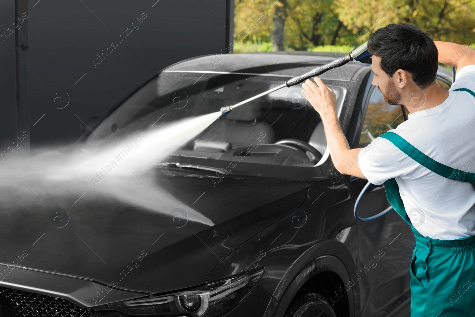 Photo of Worker washing auto with high pressure water jet at outdoor car wash