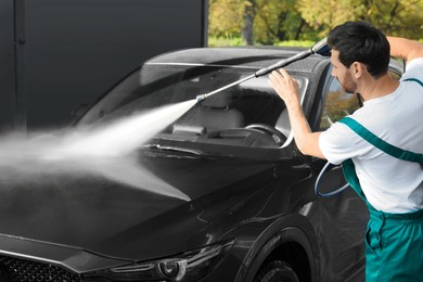 Photo of Worker washing auto with high pressure water jet at outdoor car wash