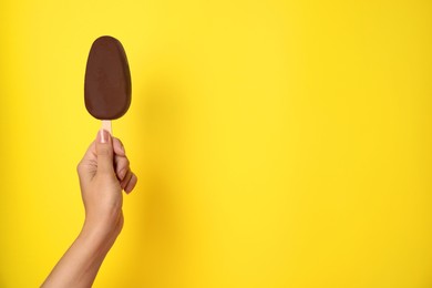 Photo of Woman holding ice cream glazed in chocolate on yellow background, closeup. Space for text