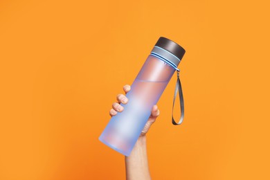 Woman holding bottle of water on orange background, closeup