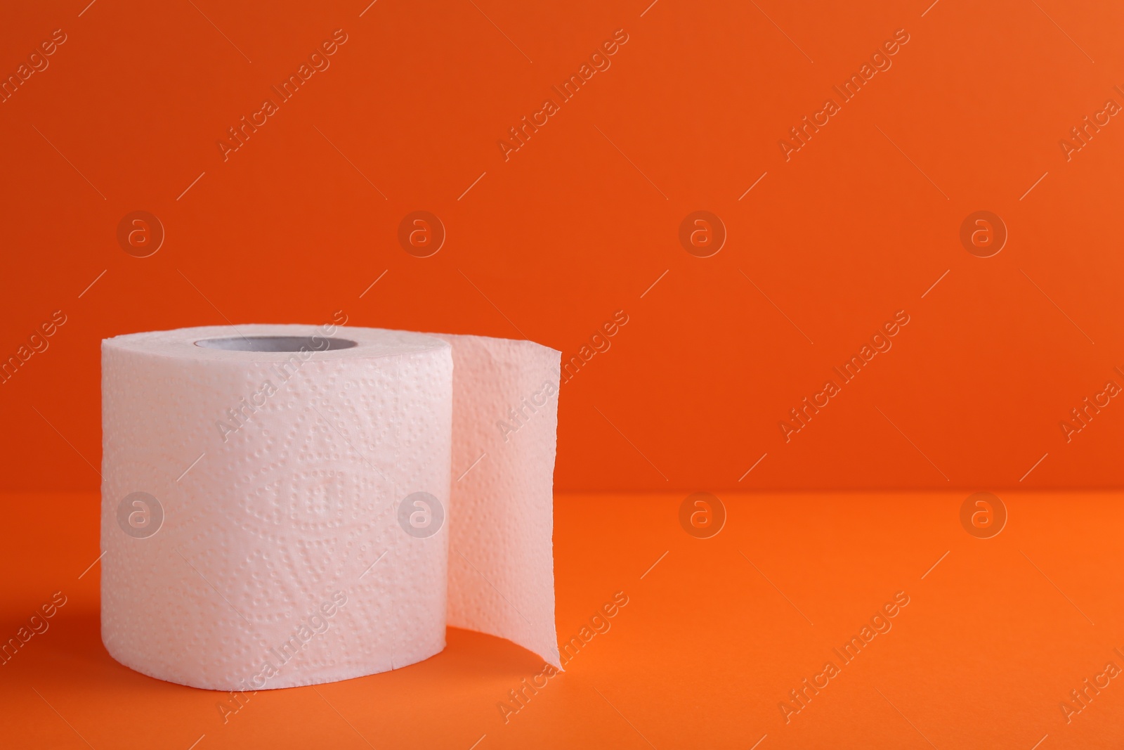 Photo of Soft toilet paper roll on orange background, closeup. Space for text