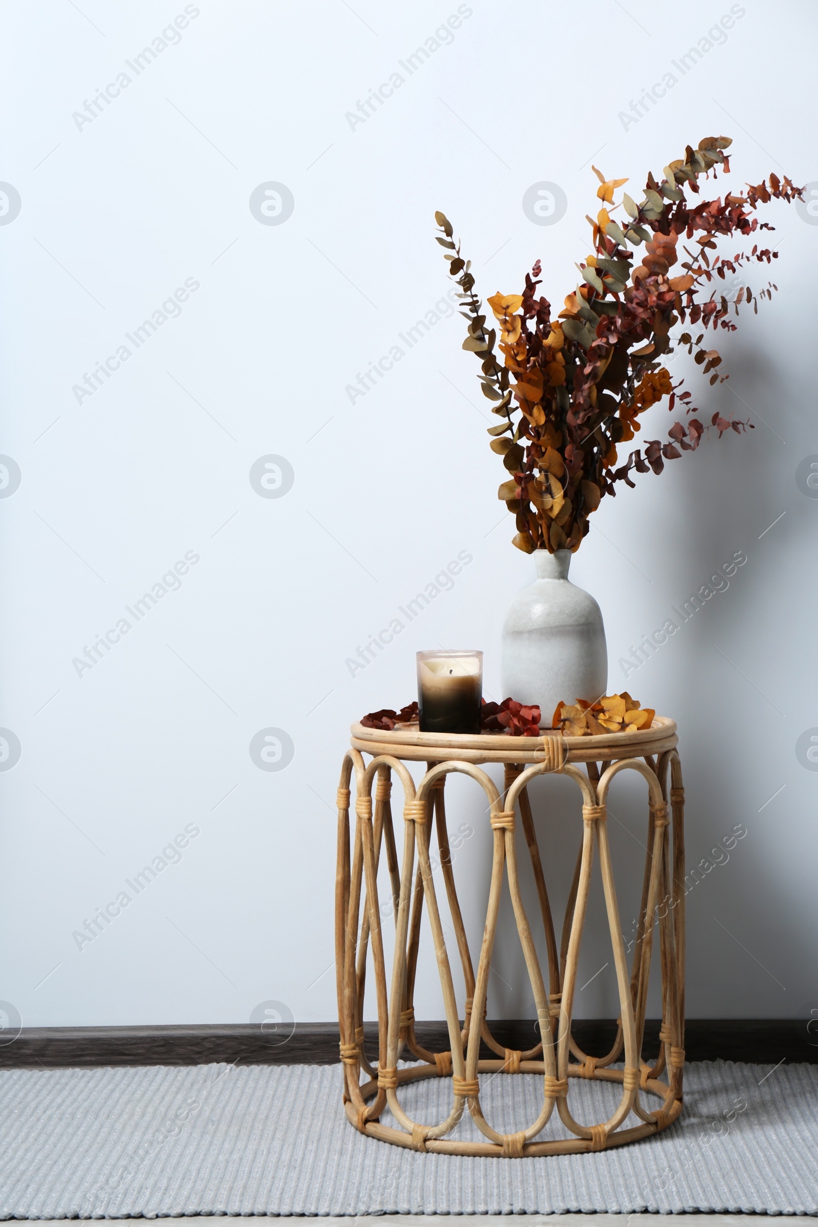 Photo of Vase with branches and candle on table near white wall, space for text