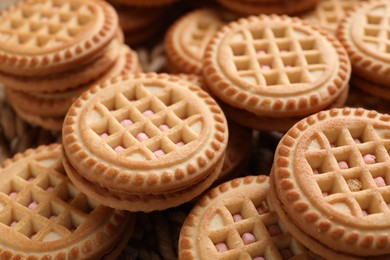 Photo of Tasty sandwich cookies with cream on wicker mat, closeup