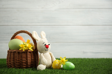 Colorful Easter eggs, rabbit and narcissus flowers on green grass against white background. Space for text