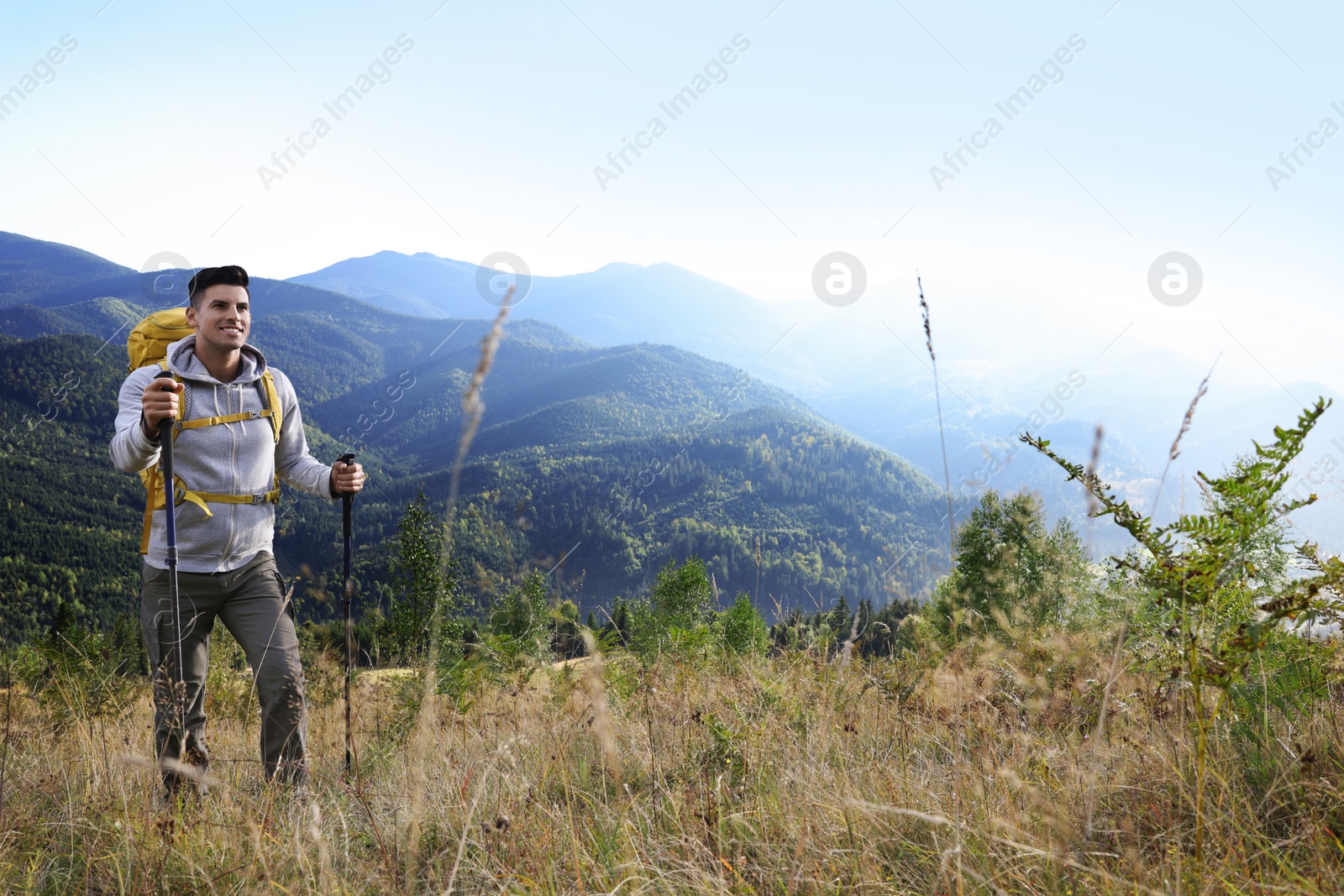 Photo of Tourist with backpack and trekking poles hiking through mountains, space for text