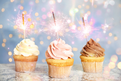 Delicious birthday cupcakes with sparklers on table against blurred lights