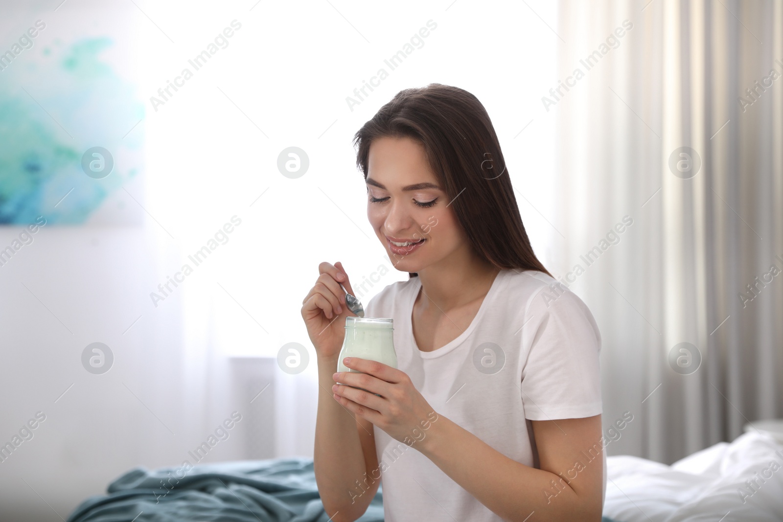 Photo of Young attractive woman with tasty yogurt on bed at home