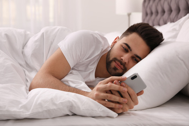 Young man addicted to smartphone in bed at home