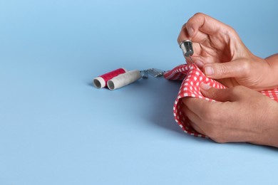 Photo of Woman sewing with thimble and needle on light blue background, closeup. Space for text