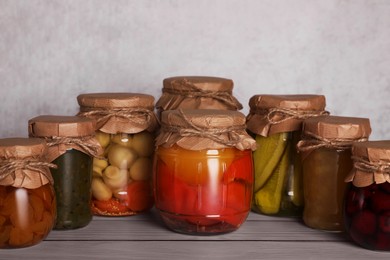 Photo of Many glass jars with different preserved products on wooden table