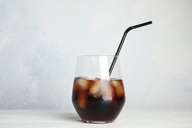 Photo of Glass of refreshing cola with ice cubes and straw on table