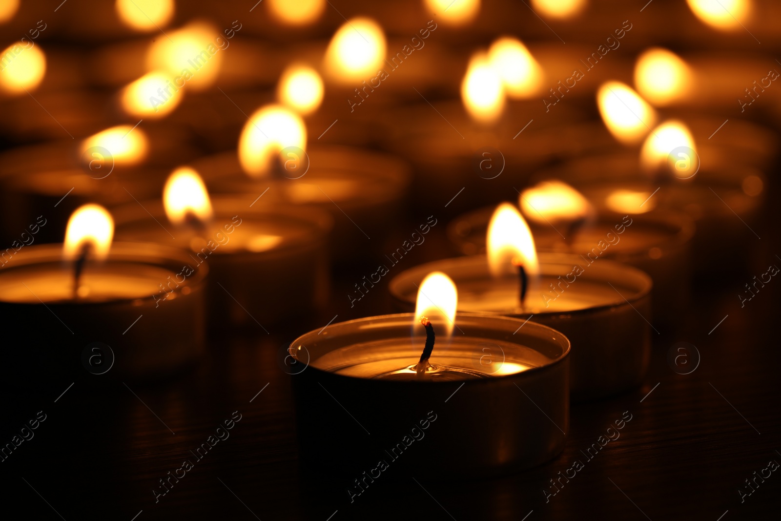 Photo of Burning candles on table in darkness, closeup