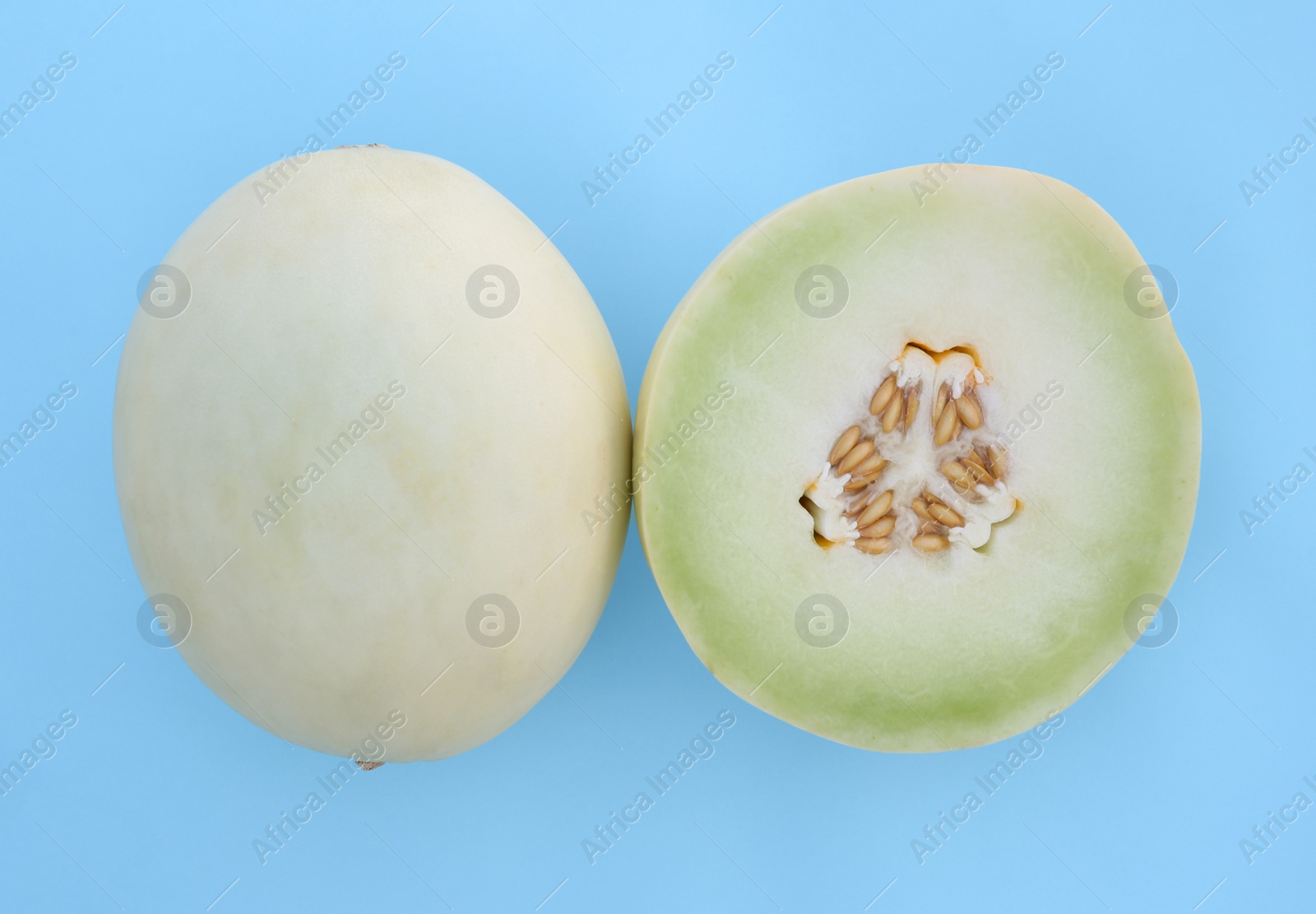 Photo of Whole and cut fresh ripe honeydew melons on light blue background, flat lay