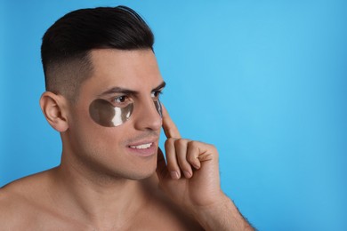 Photo of Man applying dark under eye patch on light blue background. Space for text