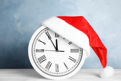 Photo of Clock with Santa hat showing five minutes until midnight on color background. New Year countdown