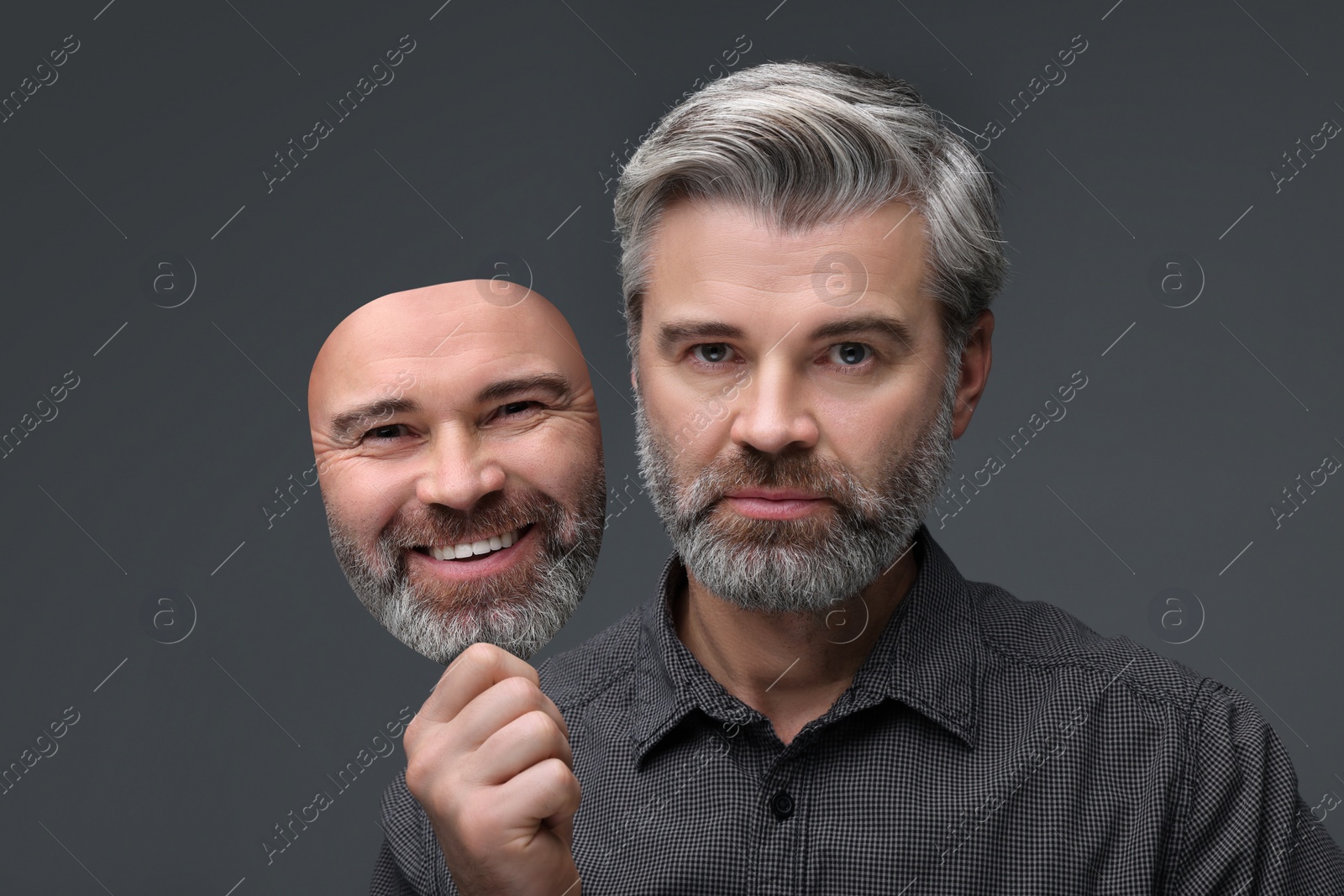 Image of Man holding mask with his facial expression on grey background. Personality crisis, different emotions