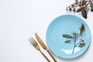 Stylish setting with cutlery and eucalyptus leaves on white background, top view. Space for text