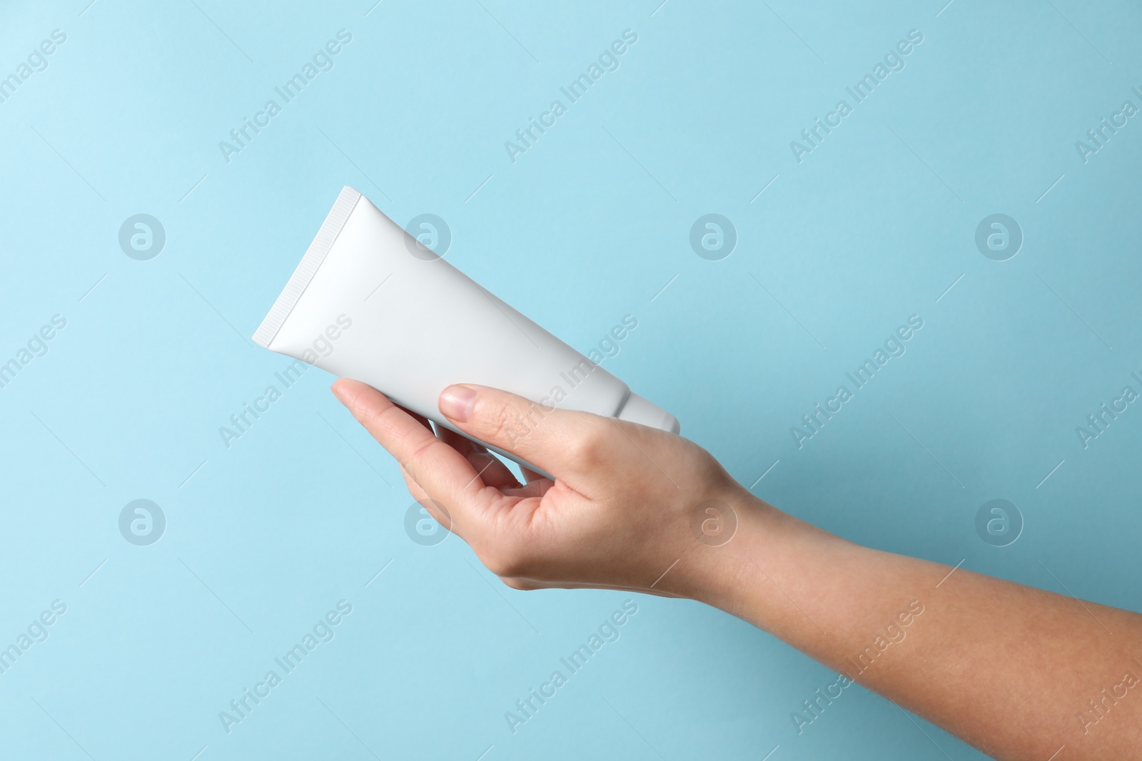 Photo of Woman with tube of hand cream on light blue background, closeup