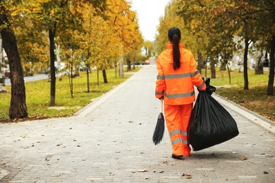 Street cleaner with broom and garbage bag outdoors on autumn day, back view
