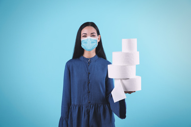 Image of Woman in medical mask holding toilet paper rolls on light blue background