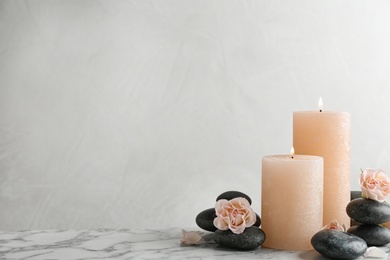 Photo of Composition of burning candles, spa stones and flowers on table. Space for text