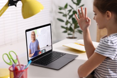 Image of E-learning. Girl raising her hand to answer during online lesson at table indoors