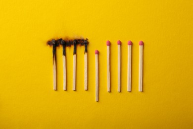 Burnt and whole matches on yellow background, flat lay. Stop destruction by breaking chain reaction concept