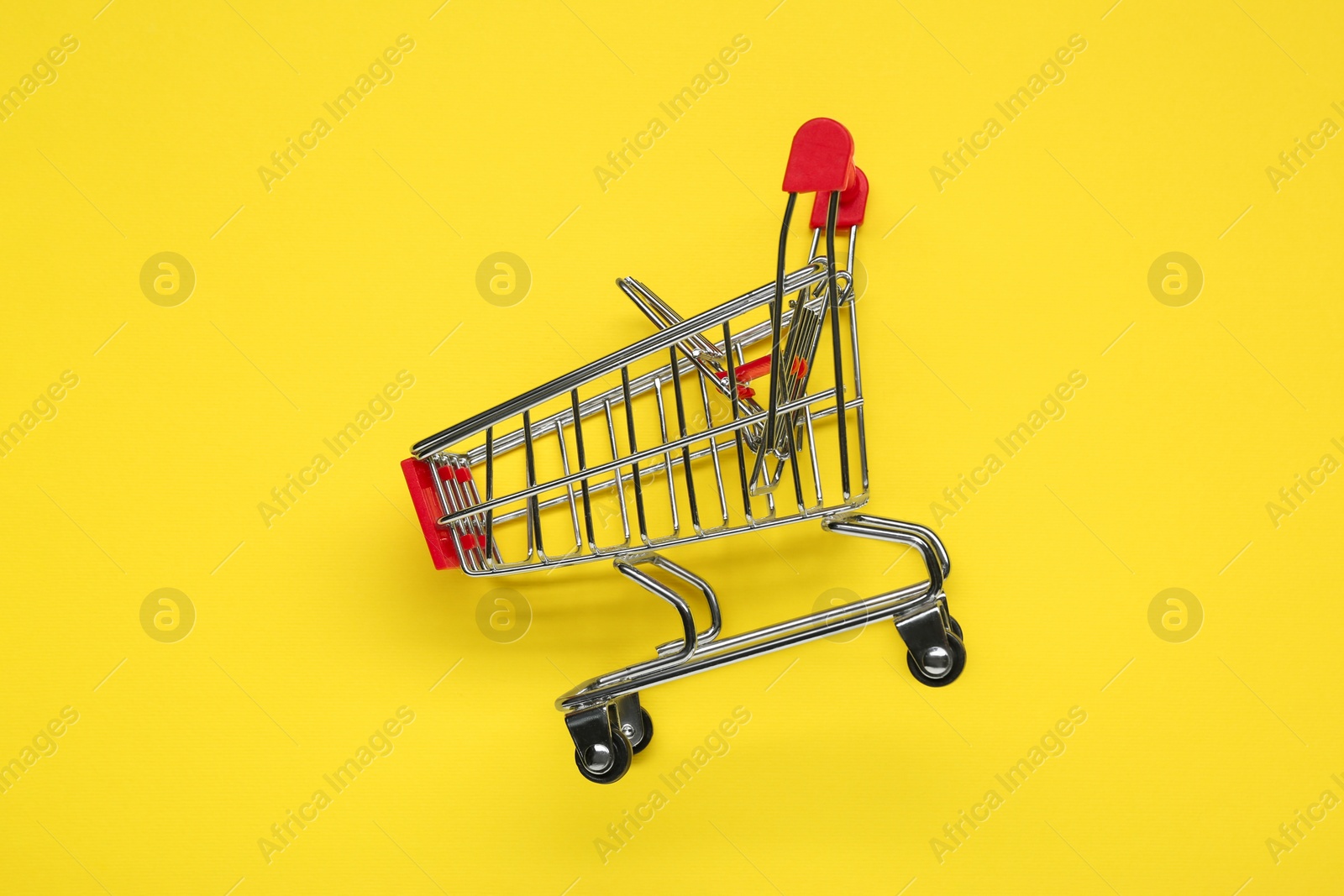 Photo of Small metal shopping cart on yellow background, top view