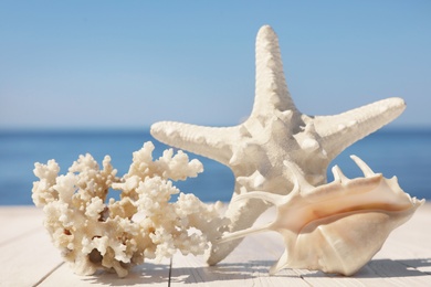 Photo of Beautiful starfish, coral and shell on wooden pier near sea, closeup