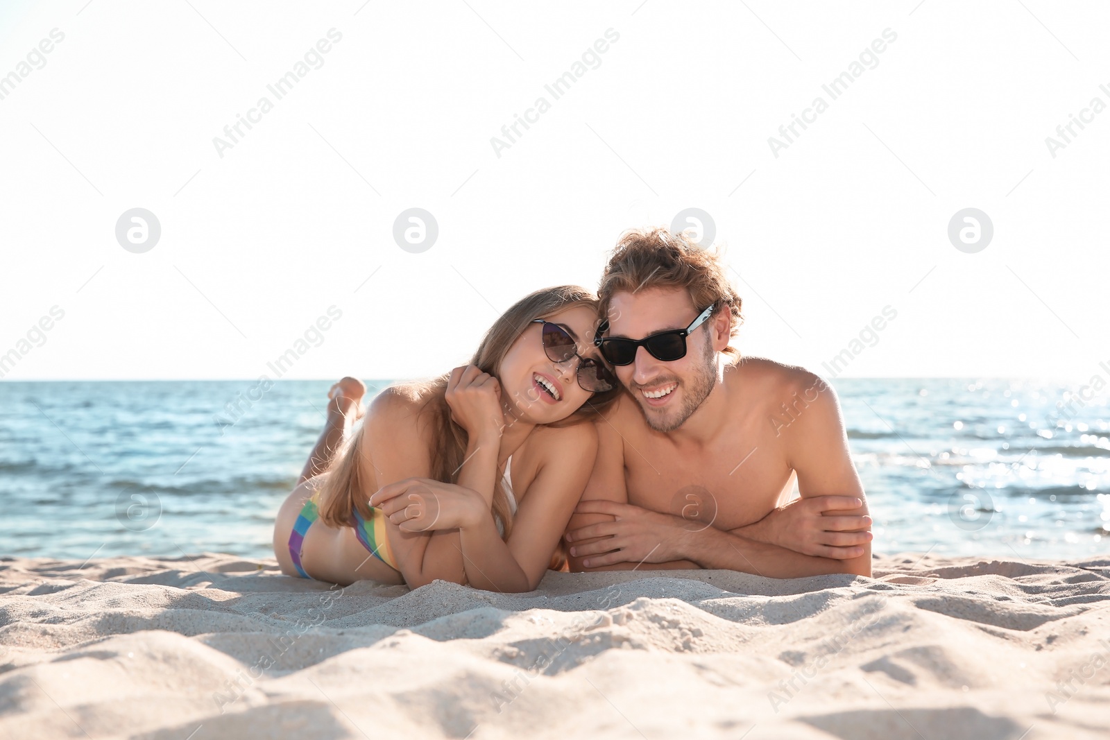 Photo of Happy young couple in sunglasses lying together on beach