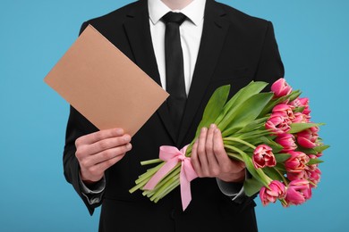 Man with beautiful bouquet and greeting card on light blue background, closeup