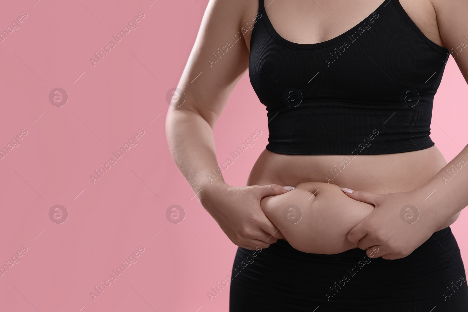 Photo of Woman touching belly fat on pink background, closeup. Overweight problem