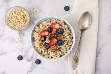 Photo of Tasty oatmeal with strawberries, blueberries and walnuts served on white marble table, flat lay