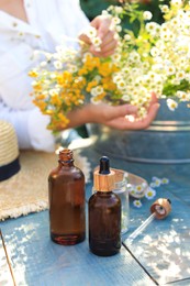 Photo of Woman with flowers near table outdoors, focus on bottles of chamomile essential oil