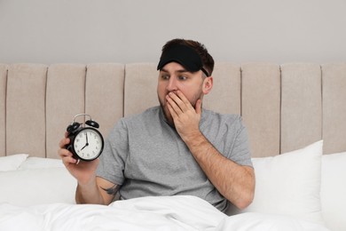 Photo of Emotional overslept man with alarm clock in bed. Being late concept