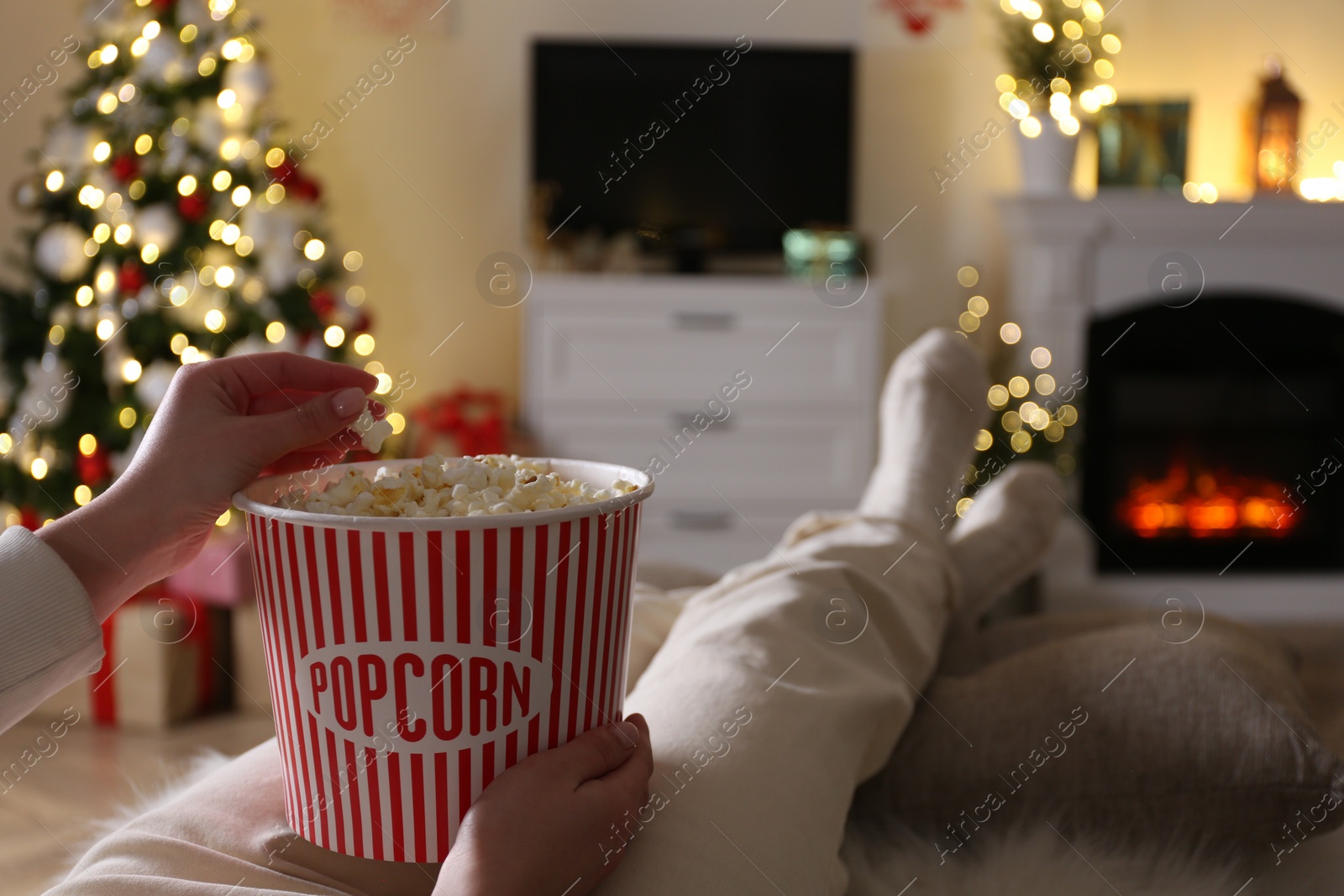 Photo of Woman with popcorn watching TV in room decorated for Christmas, closeup