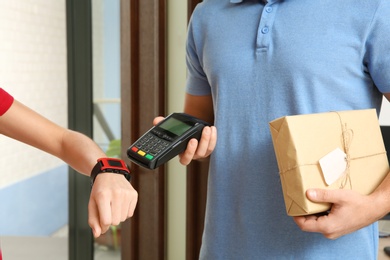 Photo of Woman with smartwatch using terminal for delivery payment indoors, closeup
