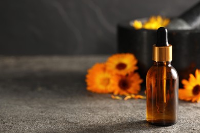 Bottle of essential oil with calendula extract on grey table, space for text