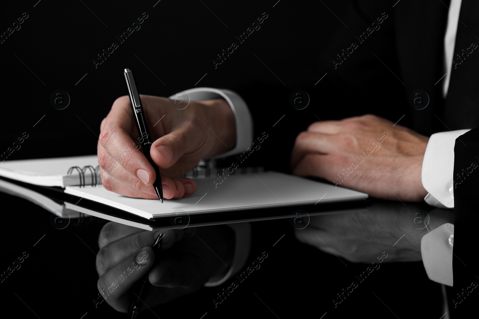 Photo of Man writing in notebook at black table, closeup