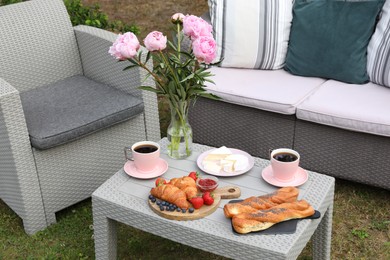 Morning drink, pastry, berries, cheese and vase with flowers on rattan table. Summer breakfast outdoors