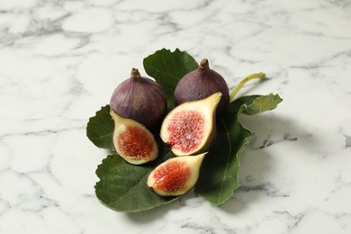 Photo of Whole and cut tasty fresh figs with green leaf on white marble table