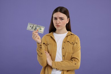 Sad woman with dollar banknote on purple background